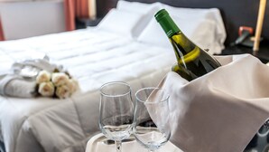 Habitación de hotel con una cama bien tendida, una botella de vino y dos copas de vino vacías sobre una bandeja.