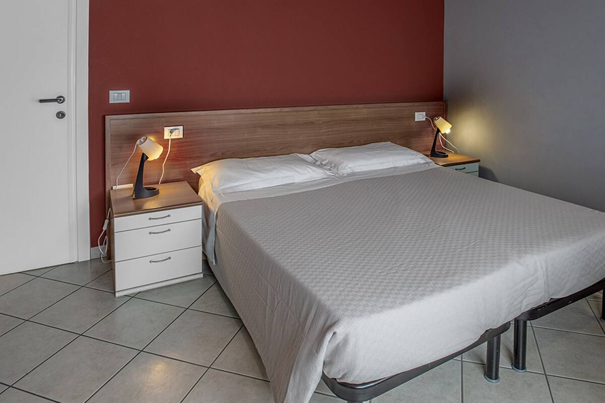 A neatly made bed with a grey bedspread, two bedside tables with lamps, a wooden headboard, and a white door.