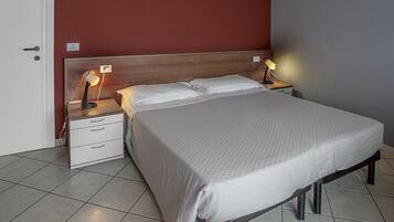 A neatly made bed with a grey bedspread, two bedside tables with lamps, a wooden headboard, and a white door.