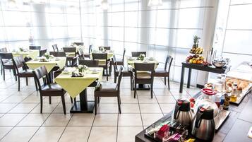 Ein geräumiger Essbereich mit mehreren Tischen und Stühlen, großen Fenstern und einem Buffet mit verschiedenen Speisen.