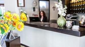 Zona de recepción con mostrador, un jarrón con girasoles, una mujer sentada y una cruz en la pared.