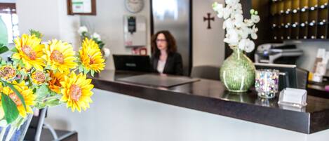 A reception area with a counter, a vase with sunflowers, a woman seated, and a cross on the wall.