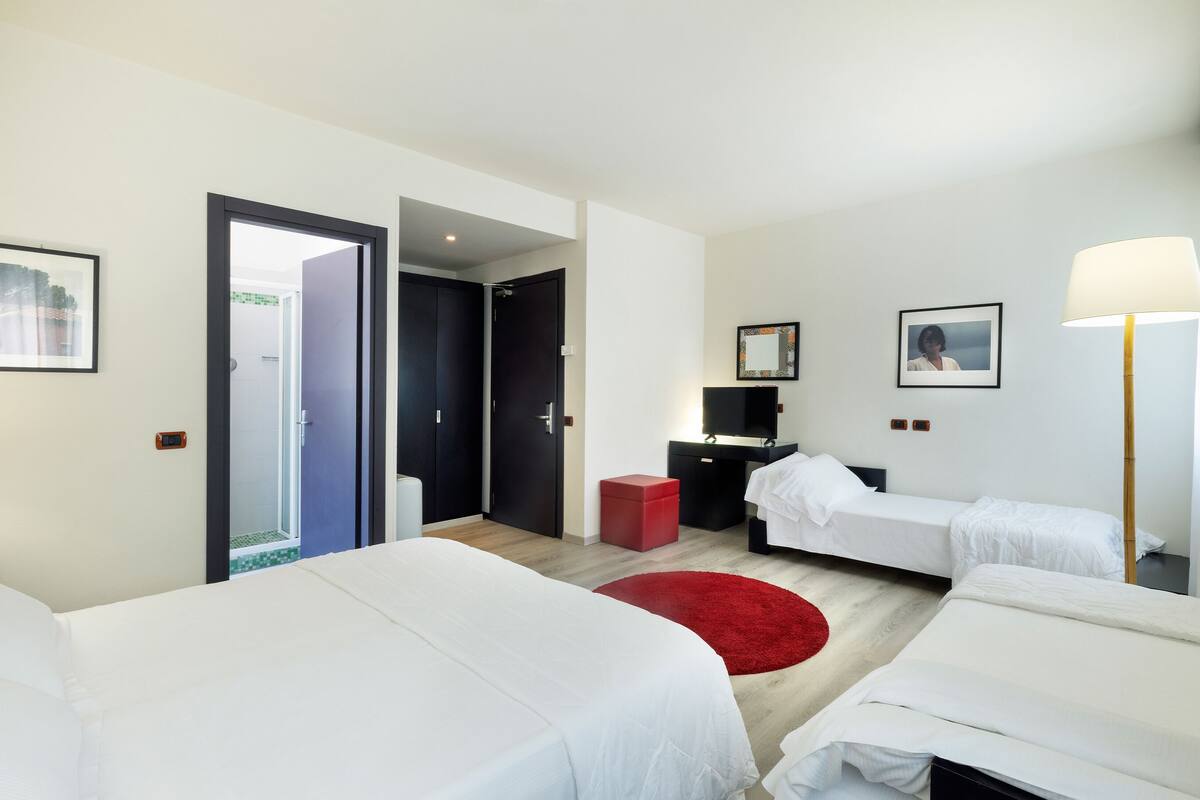 Hotellihuone, jossa on kaksi sänkyä, punainen matto, työpöytä tietokoneella, peili ja televisio.
