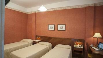 Une chambre d’hôtel avec deux lits simples, une tête de lit en bois, une table de chevet avec une lampe, un bureau avec un ordinateur portable et deux tableaux encadrés accrochés au mur.
