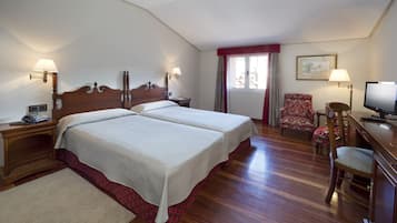 Ett hotellrum med två sängar, ett skrivbord med en tv, en stol och ett fönster med gardiner.