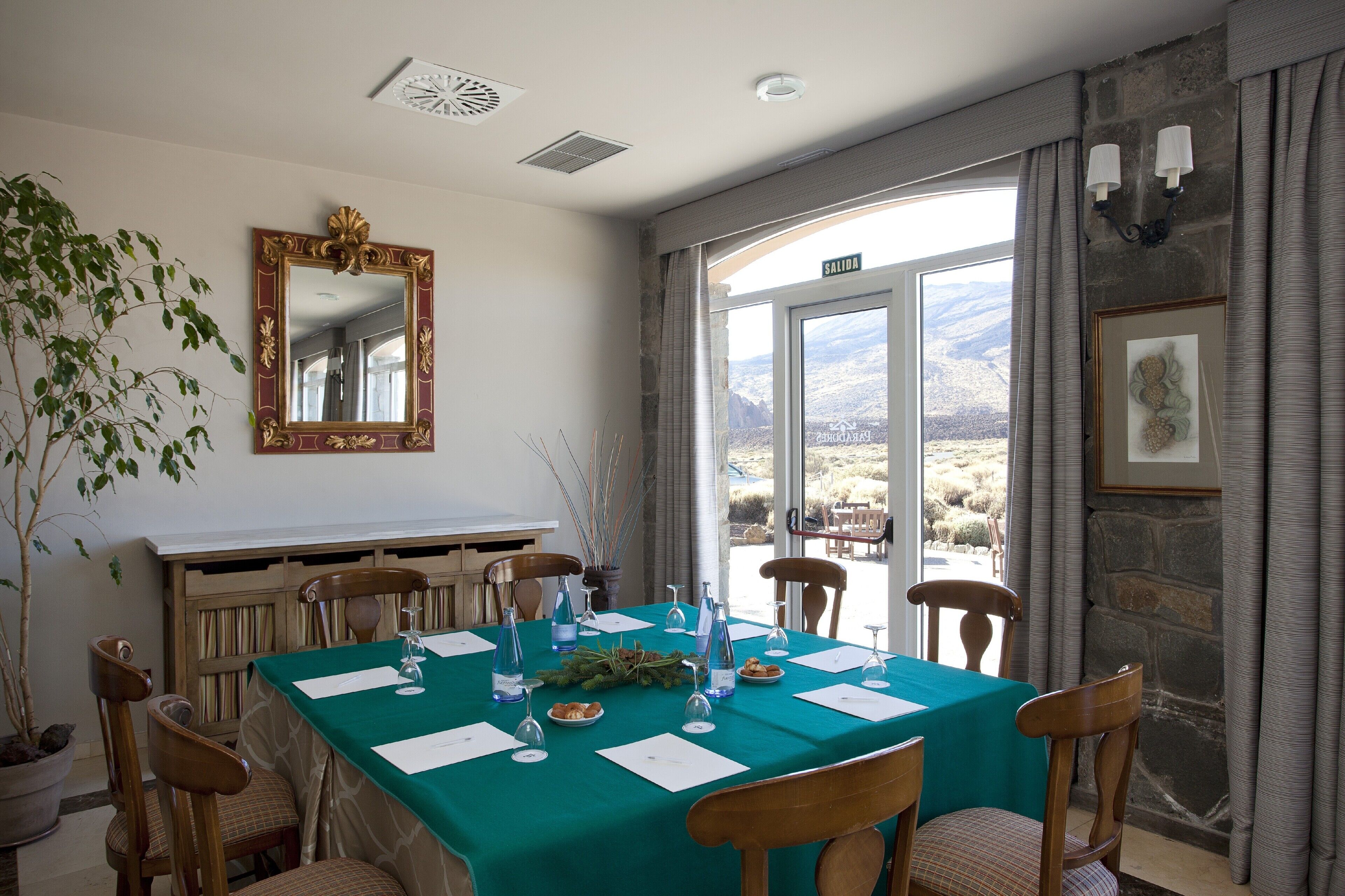 A dining room with a table set for six, a large mirror, and a view of the mountains through a glass door.