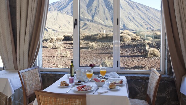 Une table de petit-déjeuner avec vue sur la montagne, une bouteille et un vase de fleurs.