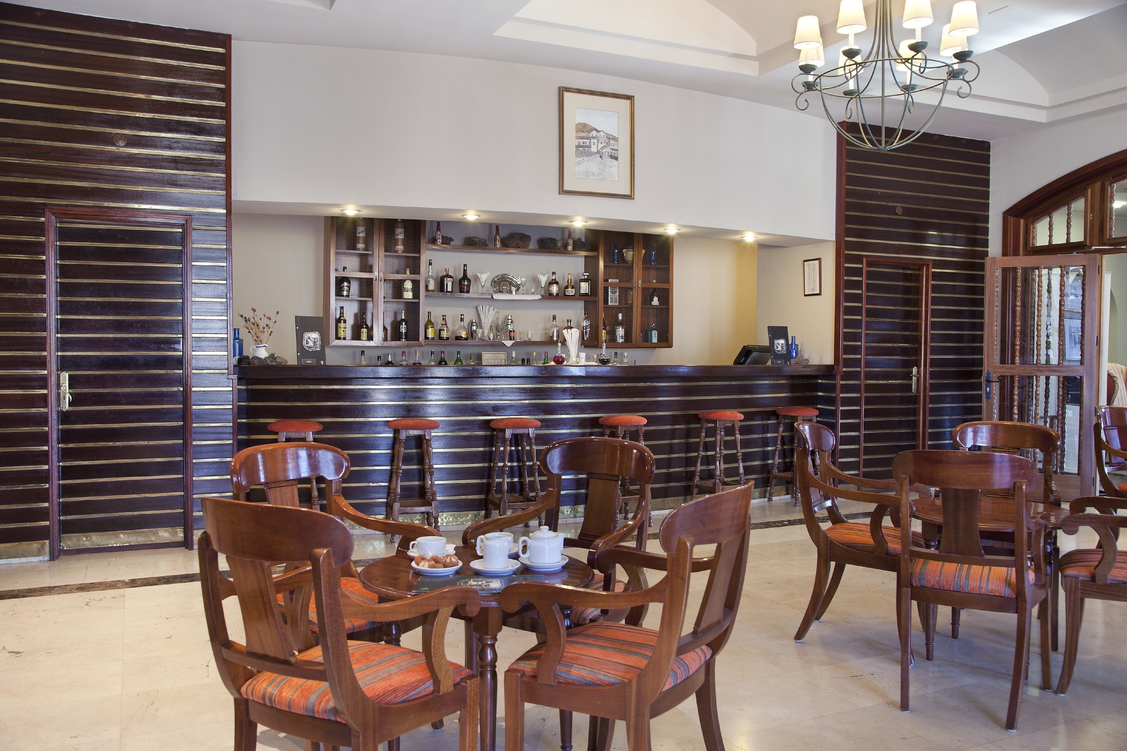 Eine Bar mit Holzsesseln, einer Theke, Regalen mit Flaschen und einem gerahmten Bild an der Wand.