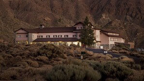 A two-story building with a flat roof, surrounded by dry shrubbery and a mountain backdrop. - Parador de las Cañadas del Teide (La Orotava)