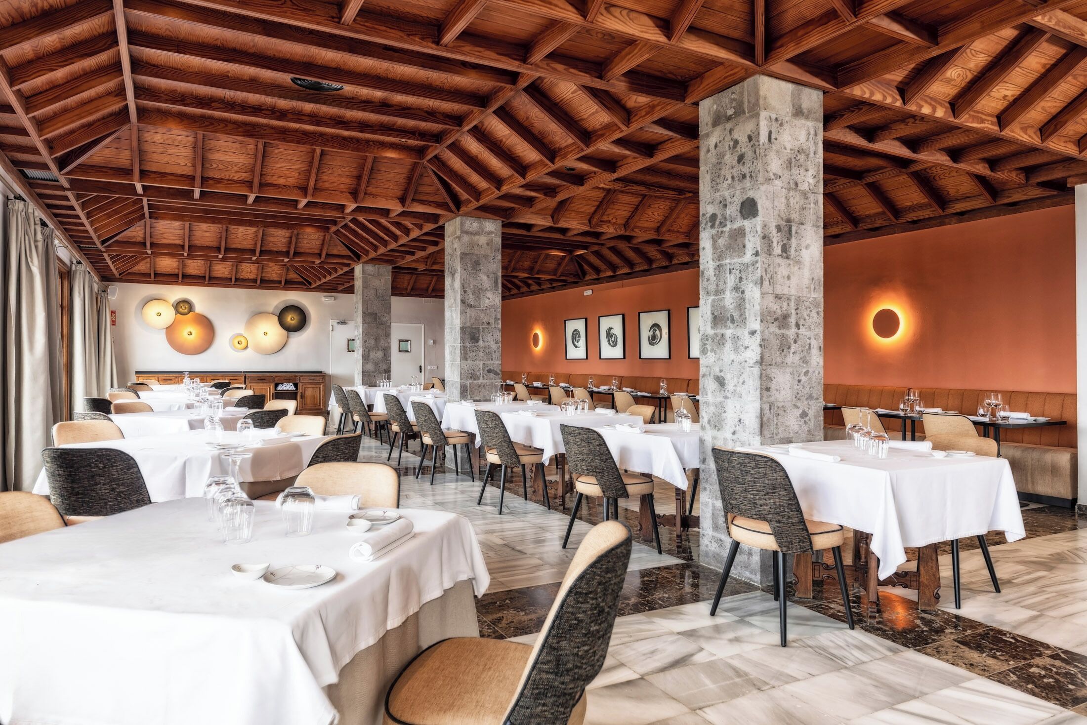 Een restaurant met meerdere tafels en stoelen, een houten plafond en een stenen zuil.
