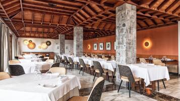 A restaurant with multiple tables and chairs, a wooden ceiling, and a stone pillar.