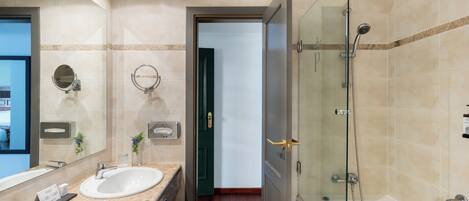 Un baño moderno con dos lavamanos, cabina de ducha de vidrio y puerta visible que da a otra habitación.