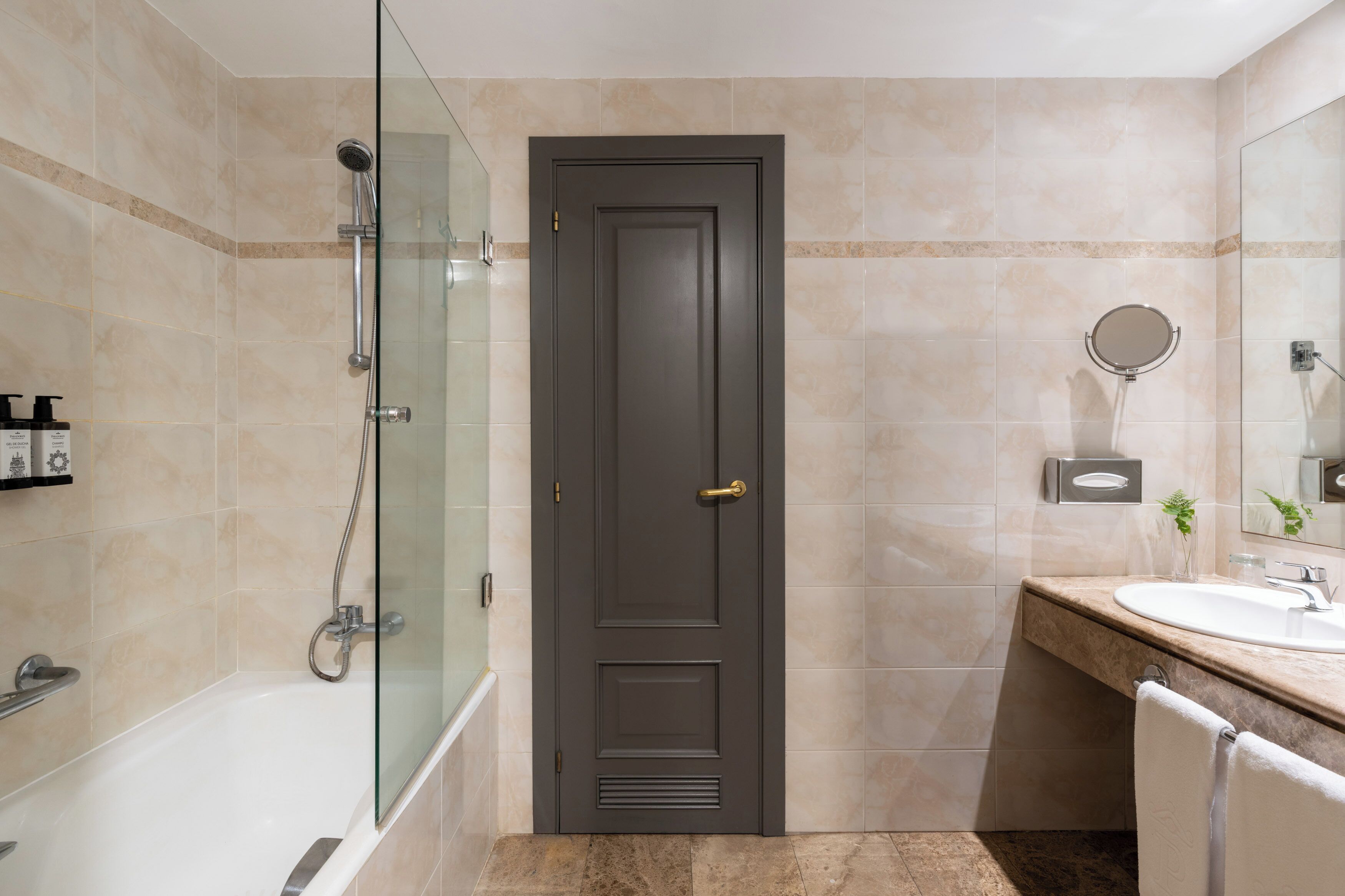 A bathroom with a bathtub, a glass-enclosed shower, a dark door, a sink with a mirror, and a towel rack.