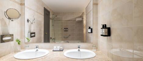 A bathroom with two sinks, a large mirror, a glass shower enclosure, and a towel rack.