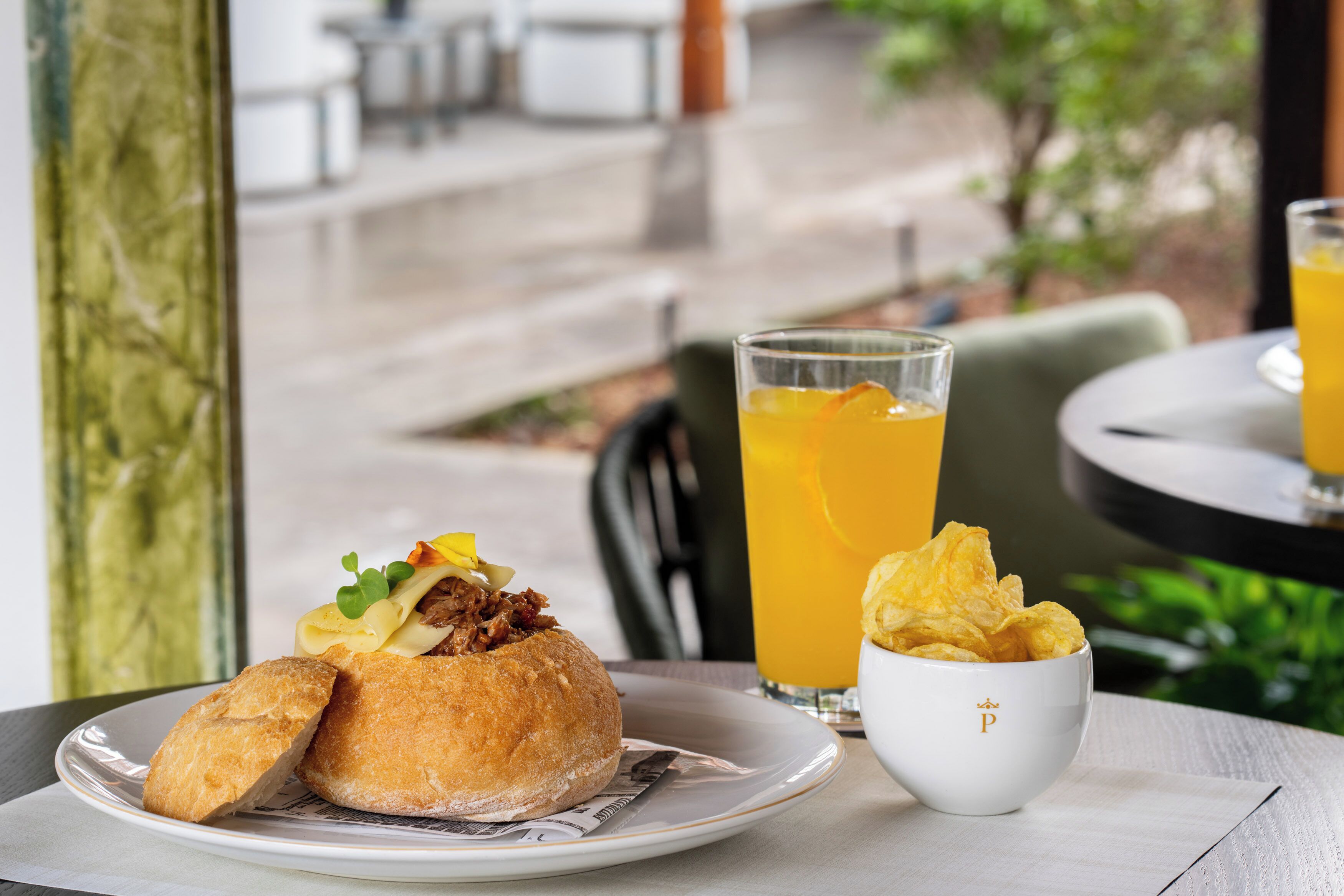 A dining table with a plate of food, a glass of orange juice, and a bowl of chips.