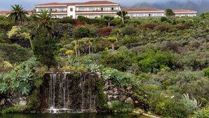 A large building with a red-tiled roof and multiple balconies, surrounded by lush greenery and a waterfall. - Parador de La Palma (Brena Baja)