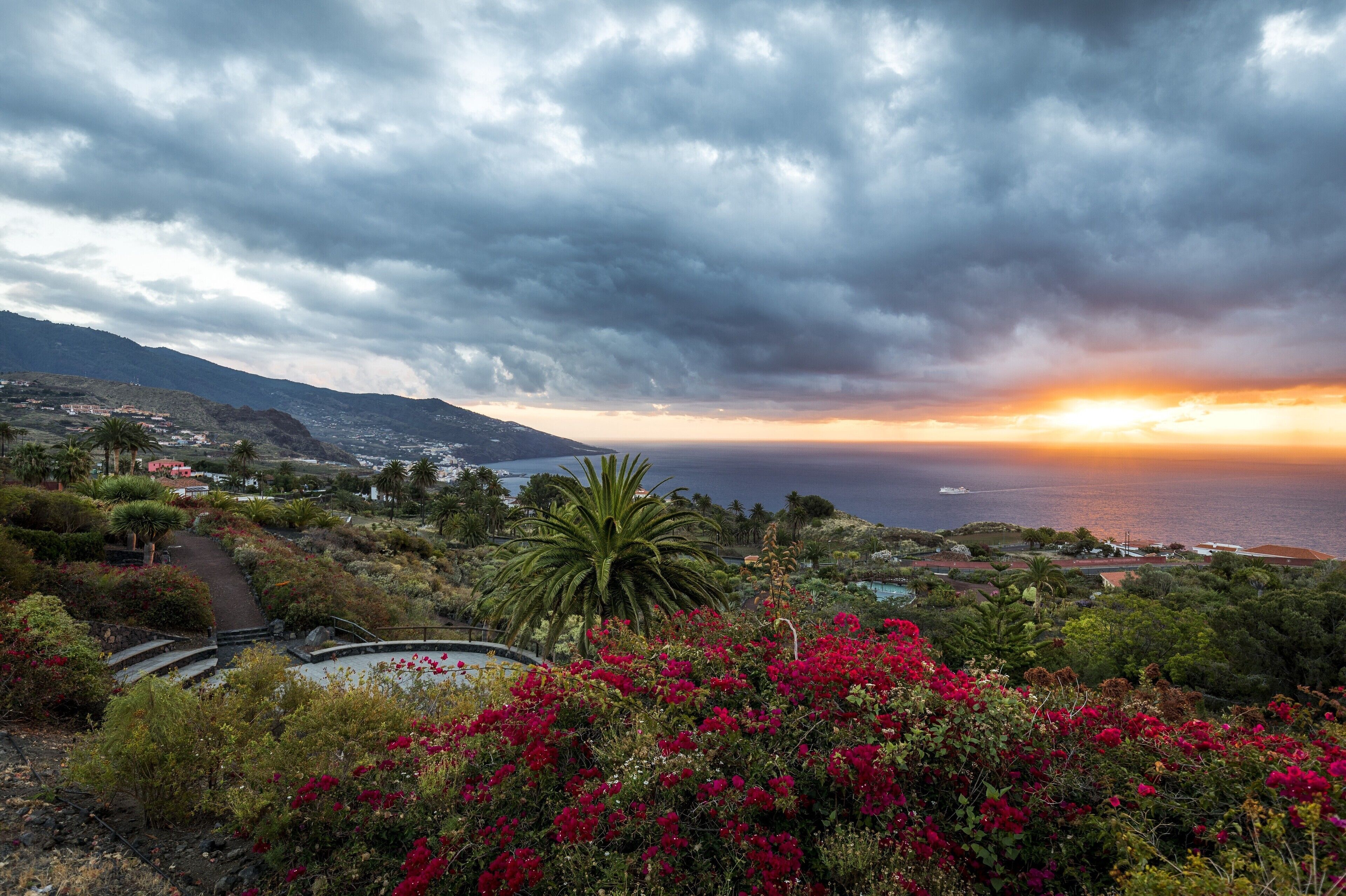 A coastal landscape with a sunset, mountains, and a pathway leading to a body of water.