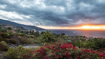 A coastal landscape with a sunset, mountains, and a pathway leading to a body of water.