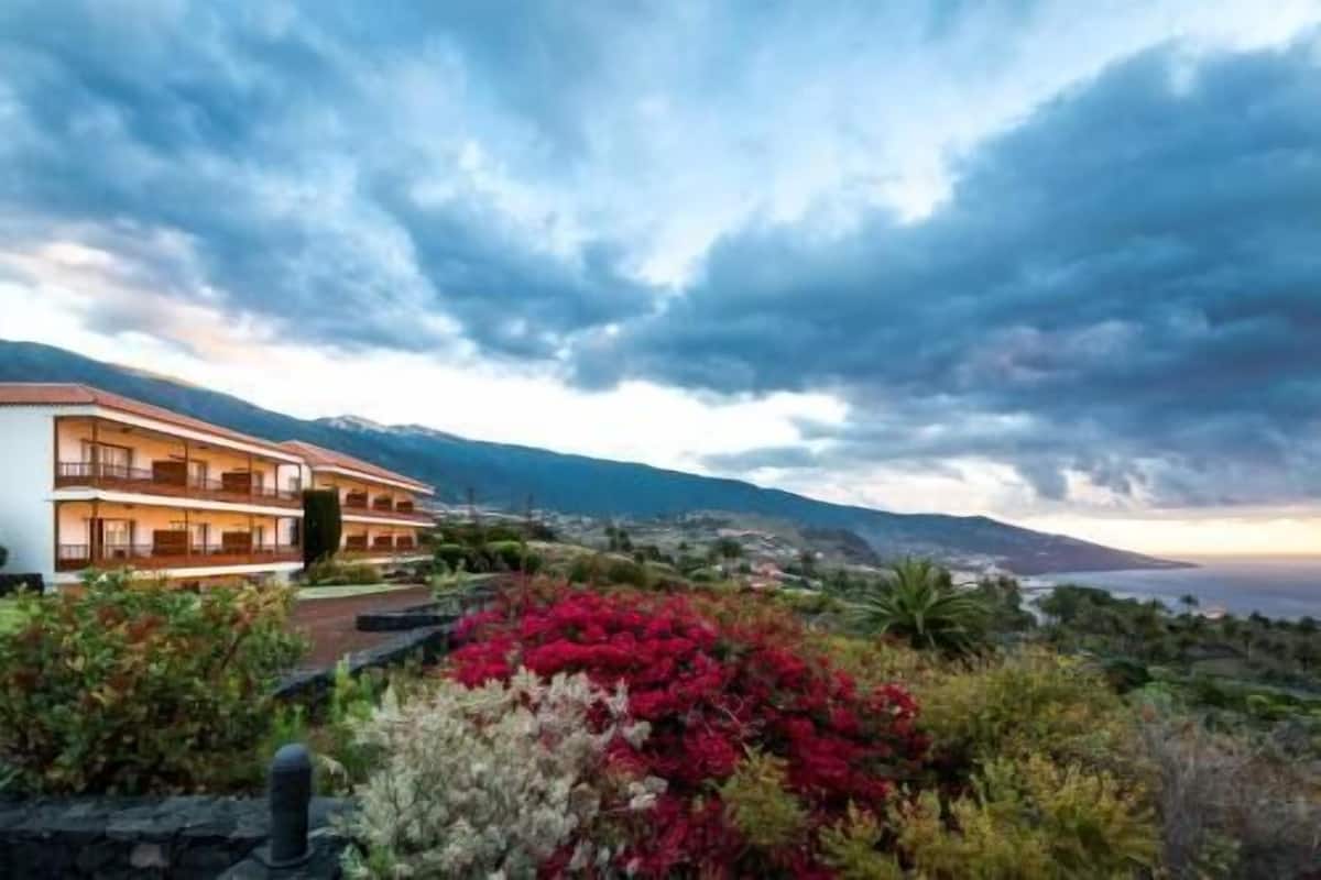 Un hotel de varios pisos con balcones, rodeado de vegetación exuberante y montañas al fondo.