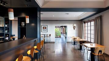 Un restaurante moderno con una zona de bar, varias mesas para comer y sillas. Se ve un jardín a través de las ventanas.