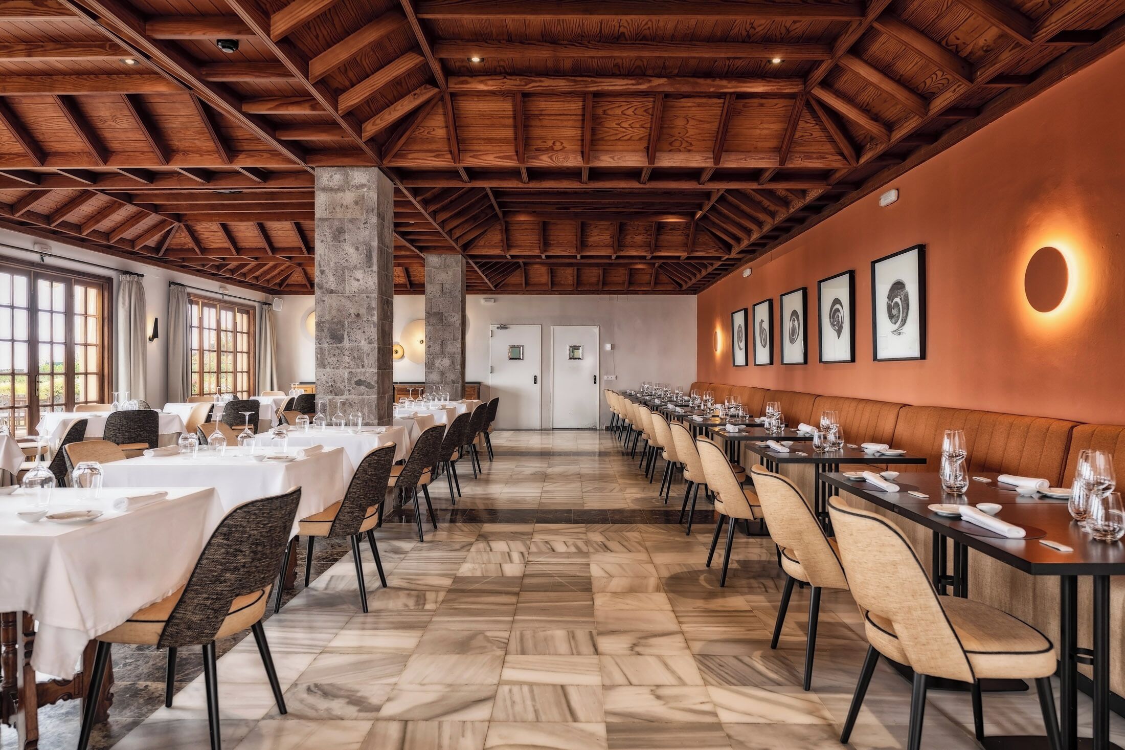 Een lange eetzaal met gedekte tafels, houten balken in het plafond en ingekaderde afbeeldingen aan de muur.