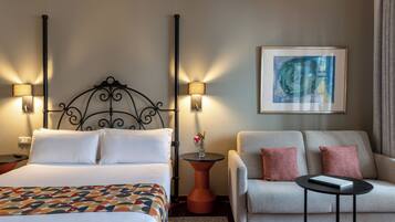 A hotel room with a bed, two bedside lamps, a sofa, a small table, and a framed artwork on the wall.