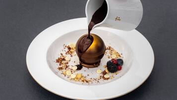 Ein Dessert auf einem weißen Teller mit goldener Kante, bedeckt mit Schokoladensauce, Beeren und zerbröselter Schokolade.