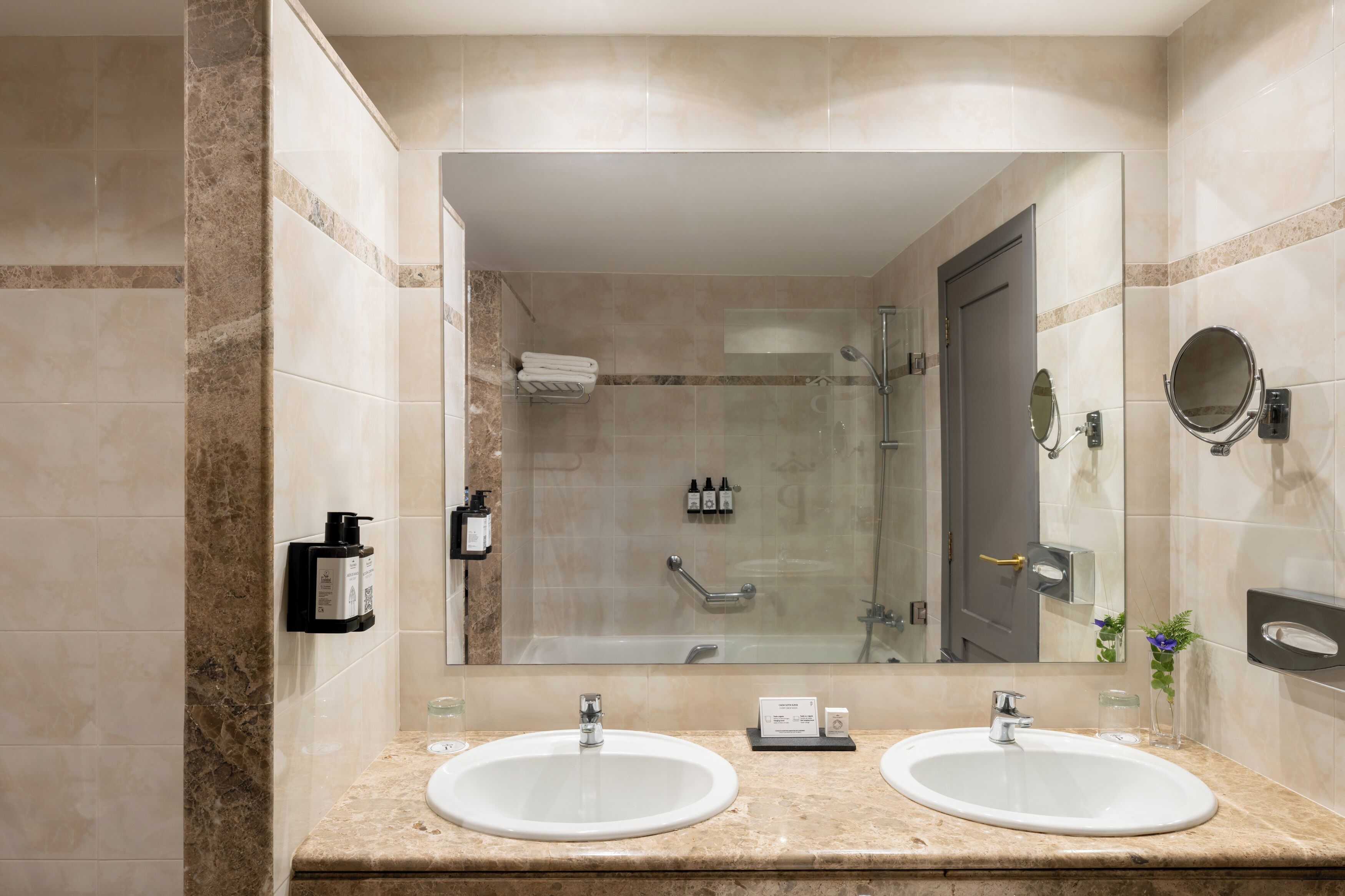 Un baño moderno con dos lavamanos, cabina de ducha de vidrio y un espejo grande.