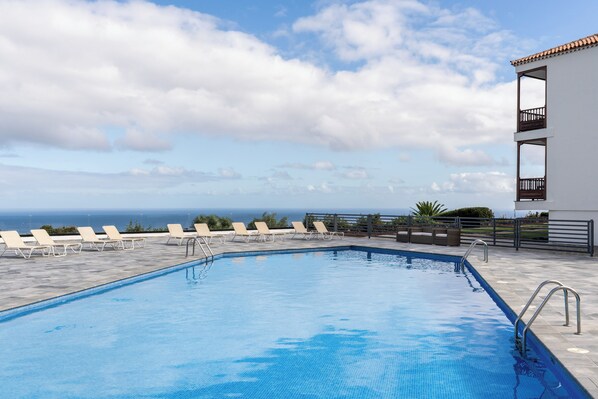 A swimming pool with lounge chairs and a view of the ocean.