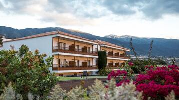 Un hotel de dos pisos con balcones, rodeado de montañas y plantas en flor.