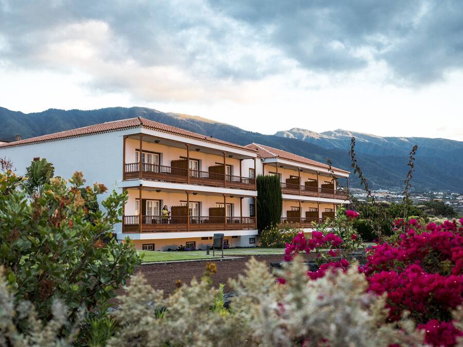 Un hotel de dos pisos con balcones, rodeado de montañas y plantas en flor.