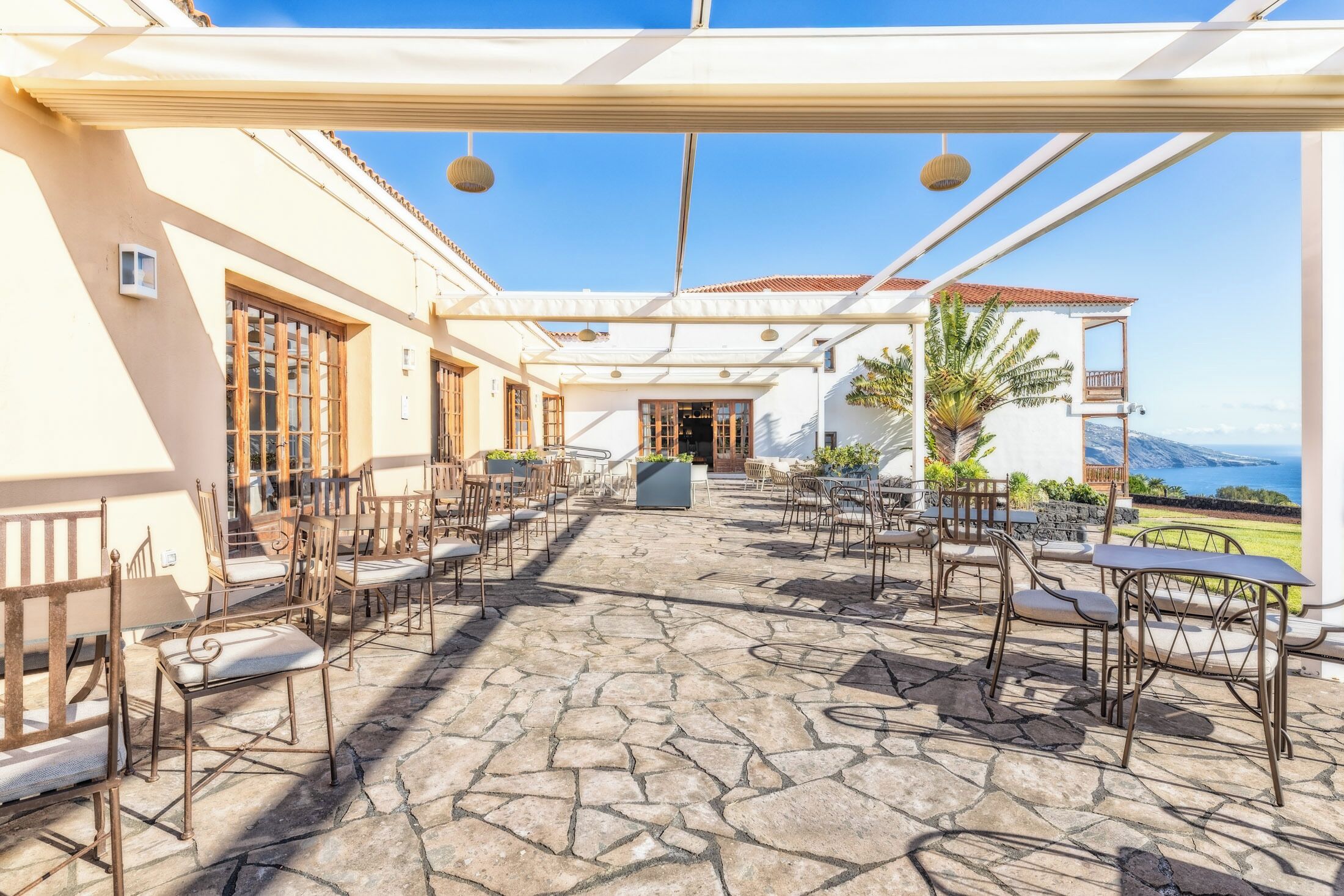 Une terrasse extérieure avec un sol en pierre et des meubles en métal, offrant une vue sur la mer et les montagnes.
