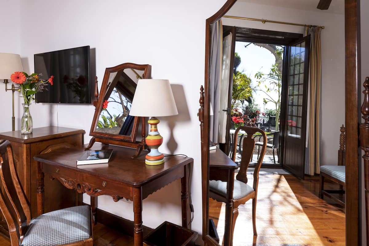 A wooden desk with a lamp, a mirror, and a vase with flowers.