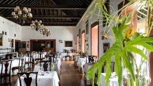 Un comedor amplio con varias mesas y sillas, una araña y obras de arte enmarcadas en las paredes.