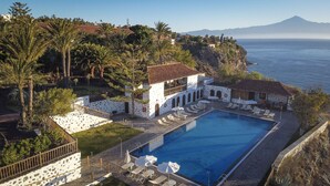 Un resort con piscina, sillas de descanso y vistas al océano y a la montaña.
