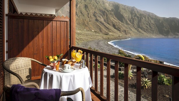 A balcony with a table set for breakfast overlooking a beach with mountains in the background. - Parador de El Hierro (Valverde)