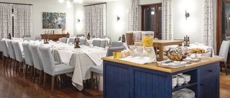A dining area with multiple tables set for a meal, a buffet station, and a wooden cabinet with dishes.