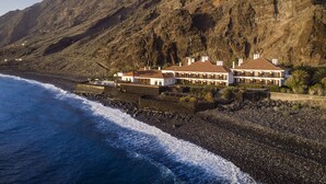 A coastal property with a large house featuring multiple balconies, situated on a rocky beach with a view of the ocean and a mountainous backdrop. - Parador de El Hierro (Valverde)