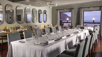 Een restaurant met meerdere tafels, grote ramen met uitzicht op zee en een modern interieur.