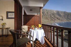 A balcony with wicker chairs, a table with a white tablecloth, and a view of the ocean and mountains. - Parador de El Hierro (Valverde)