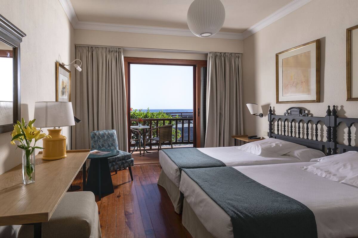 Ein Hotelzimmer mit zwei Betten, einem Schreibtisch, einem Stuhl, einem Tisch und einem Balkon mit Blick.