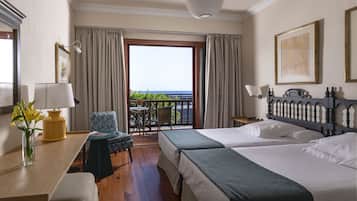 A hotel room with two beds, a desk, a chair, a table, and a balcony with a view.