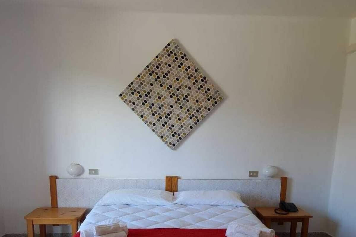 Un lit bien fait, avec une couverture rouge et deux oreillers, une tête de lit en bois, deux tables de chevet avec des lampes et un objet décoratif fixé au mur.