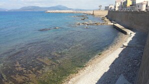 A coastal area with clear water, a rocky shoreline, and buildings along the shore. - Hotel Mistral (Alghero)