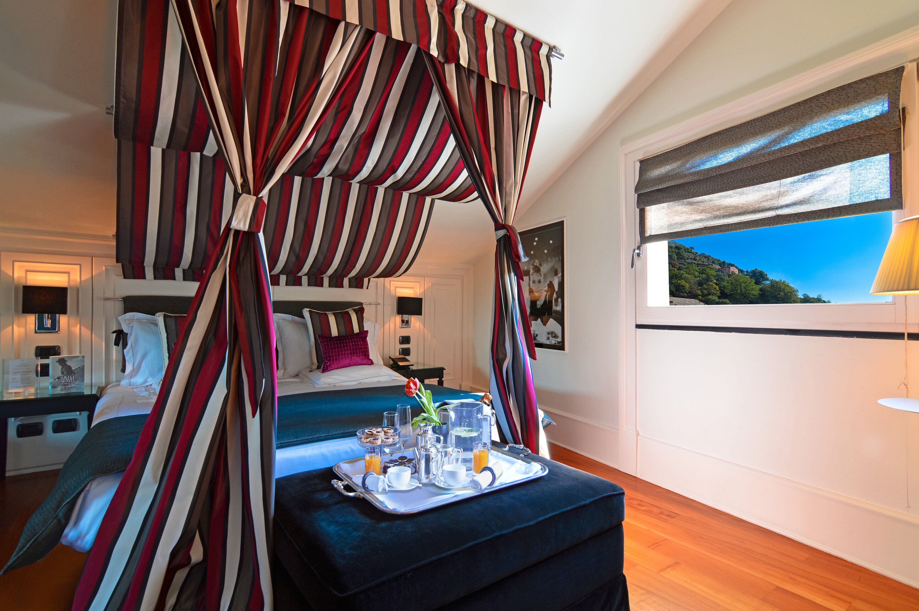 A hotel room with a bed, a tray with breakfast items, and a window with a view of a mountain.