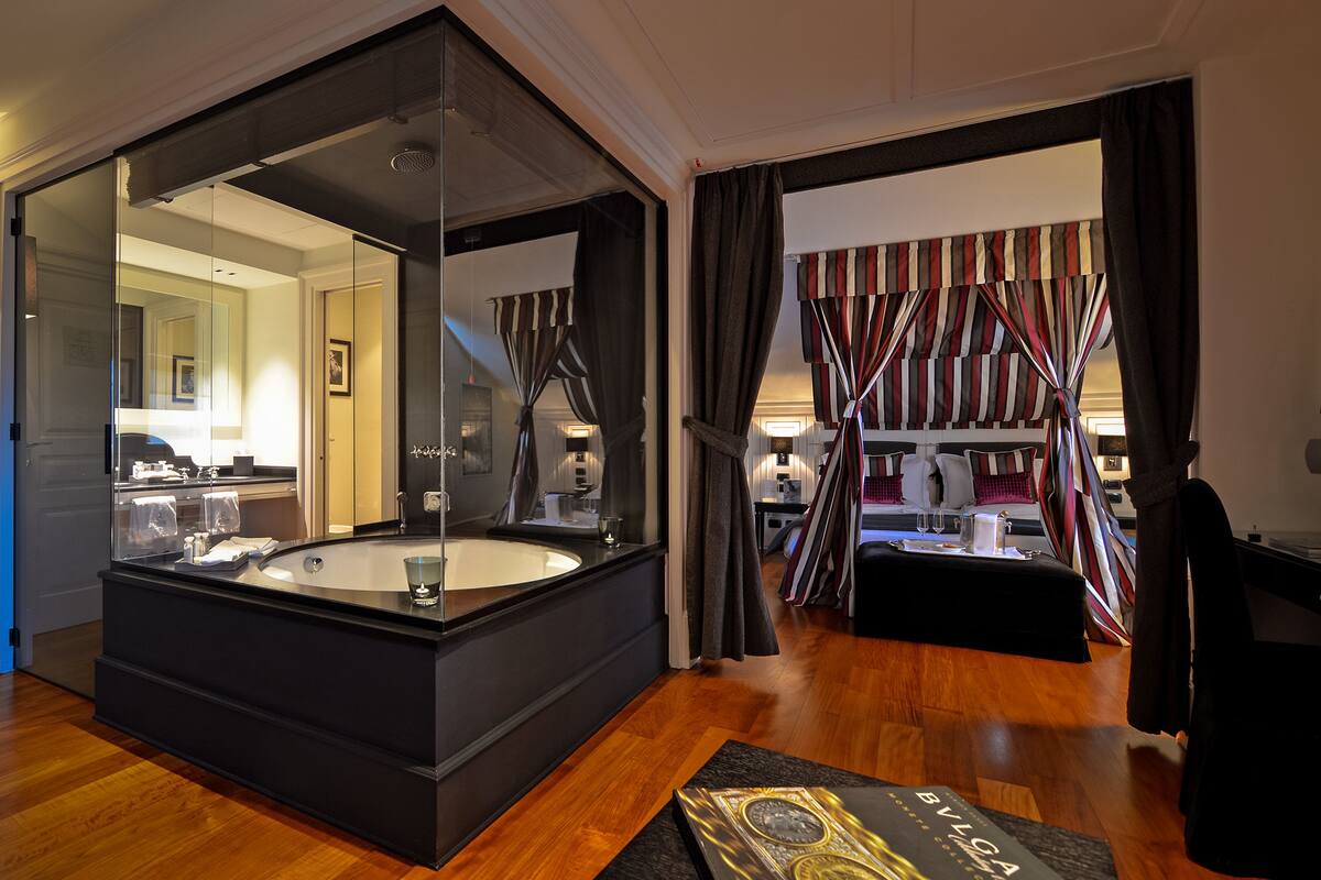 Ein modernes Hotelzimmer mit einer großen Badewanne, einem Flachbildfernseher und einer gemütlichen Sitzecke mit gestreiften Vorhängen.
