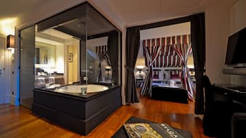 A modern hotel room with a large bathtub, a flat-screen TV, and a cozy seating area with striped curtains.