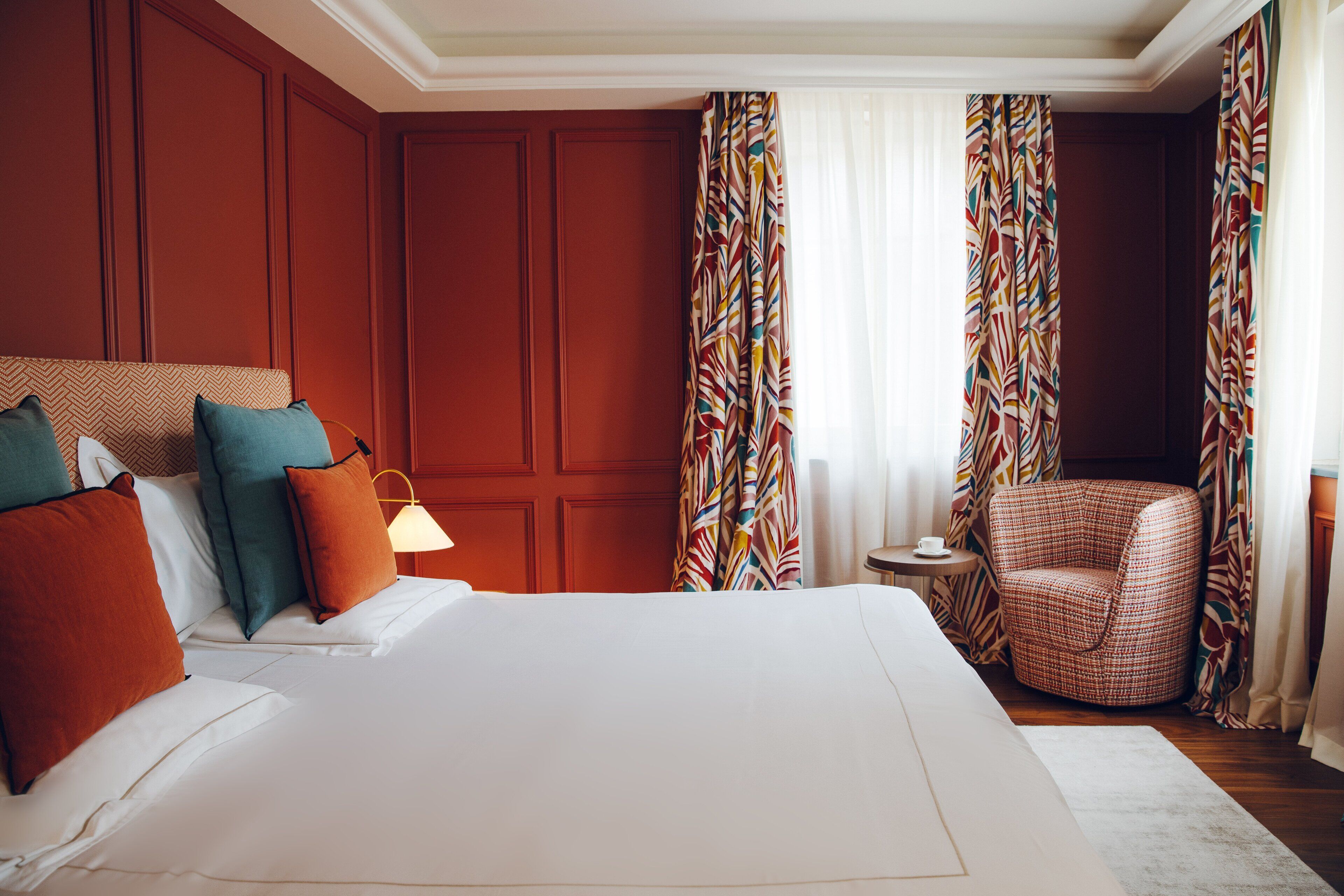 Ein Hotelzimmer mit einem großen Bett, vielen Kissen, einem Sessel, einem kleinen Tisch und Vorhängen.