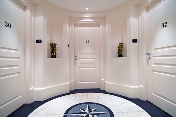A hotel corridor with doors numbered 30, 31, and 32, featuring a marble floor and a central decorative element.