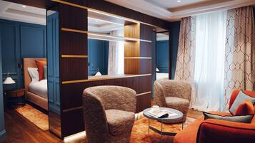A modern hotel room with a bed, two armchairs, a sofa, a small table, and a built-in wardrobe.